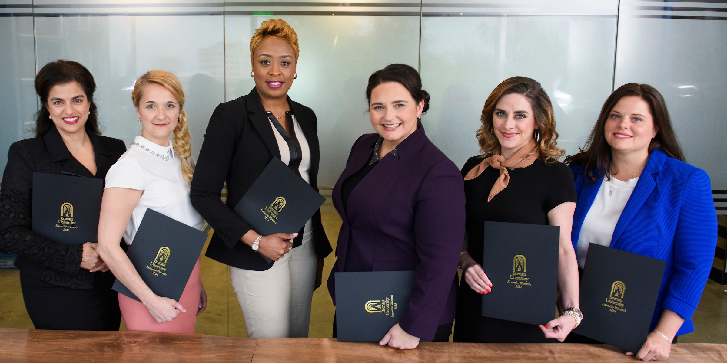 Row of professional, women executives holding folders with Brenau logo